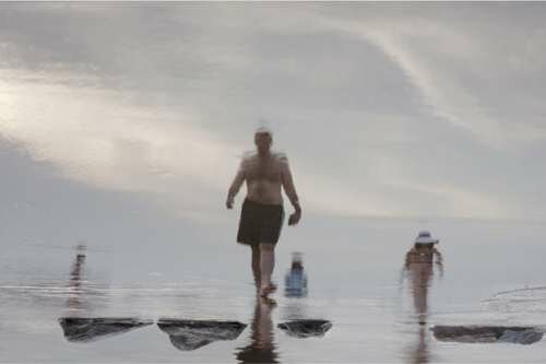 Through reflections of beachgoers seen in the wet sands