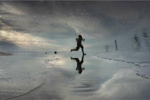 Through reflections of beachgoers seen in the wet sands